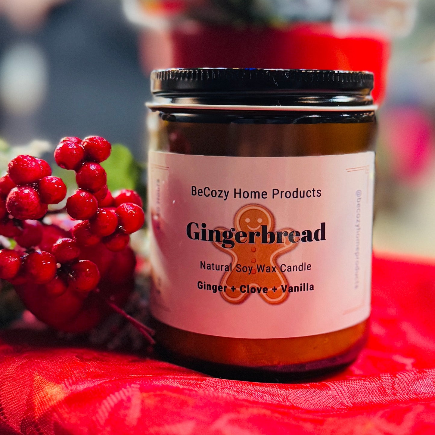 A Gingerbread Soy Wax Candle with a red lid and label, displayed on a red cloth surface.