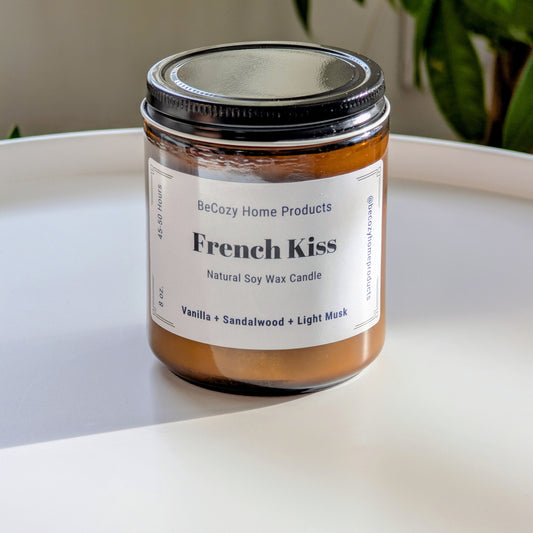 BeCozy Home Products soy wax candle labeled 'French Kiss' on a white surface with a plant in the background.