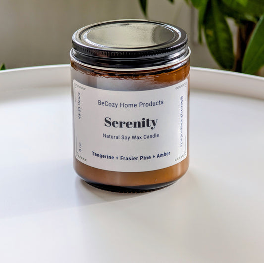 Serenity soy wax candle by BeCozy Home Products on a white surface with a plant in the background